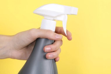 Sarı arka planda plastik sprey şişesi tutan kadın, yakın plan. Metin için boşluk