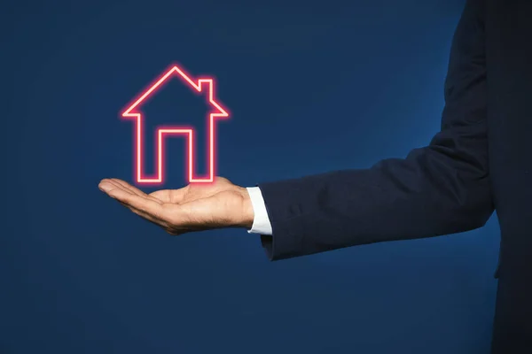 Mortgage rate. Man holding illustration of house on dark blue background, closeup