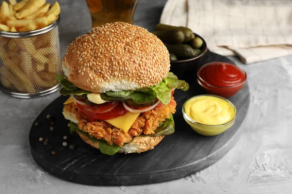 Delicious burger with crispy chicken patty and sauces on grey table, closeup