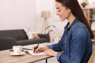 İçerideki ahşap masada deftere yazı yazan genç bir kadın.