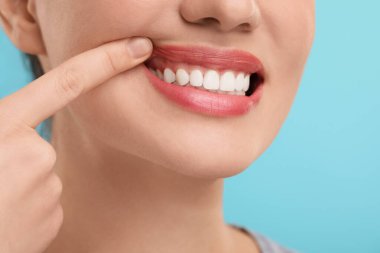 Açık mavi arka planda temiz dişlerini gösteren kadın, yakın plan.