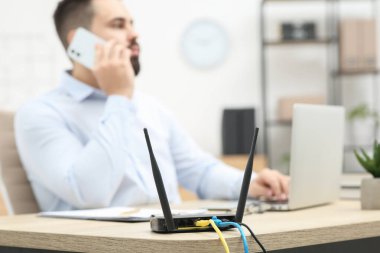 Ahşap masada çalışırken akıllı telefondan konuşan adam, Wi-Fi yönlendiricisine odaklan.