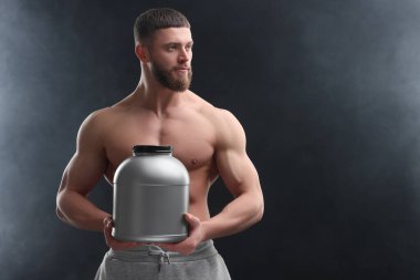 Kas yığını bir kavanoz protein tozunu koyu gri arka planda tutan genç bir adam.
