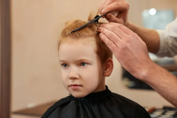 Professional hairdresser combing boy's hair in beauty salon, closeup