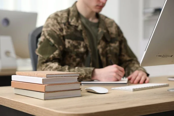 Military education. Student in soldier uniform learning at wooden table indoors, selective focus
