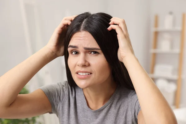 Emotional woman examining her hair and scalp in bathroom. Dandruff problem