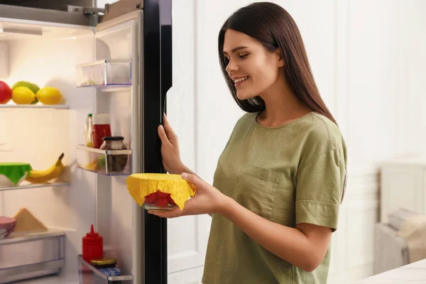 stock image Woman holding bowl of fresh tomatoes covered with beeswax food wrap near refrigerator in kitchen