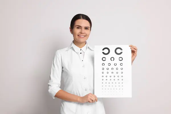 Ophthalmologist with vision test chart on light background