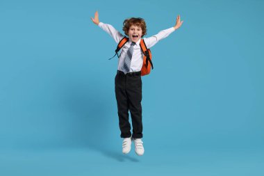 Sırt çantalı, açık mavi arka planda zıplayan mutlu okul çocuğu.