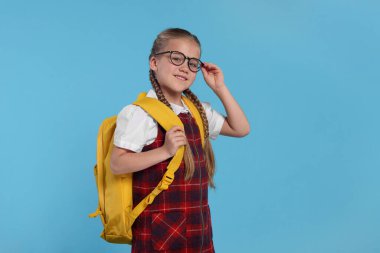 Açık mavi arka planda sırt çantalı, gözlüklü mutlu kız öğrenci.
