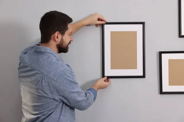 Man hanging picture frame on gray wall