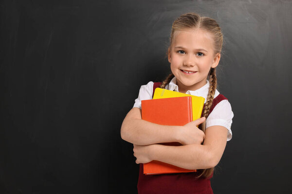 Happy schoolgirl with books near blackboard, space for text
