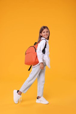 Turuncu arka planda sırt çantası olan mutlu bir kız öğrenci.