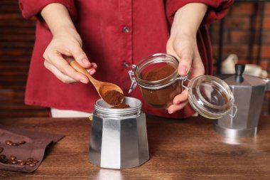 Ahşap masada kahve demliğine öğütülmüş kahve koyan kadın.