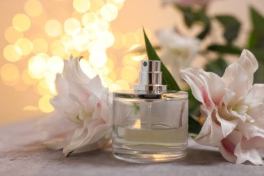 Bir şişe parfüm ve güzel zambak çiçekleri bej arka planda bulanık ışıklarla, yakın plan