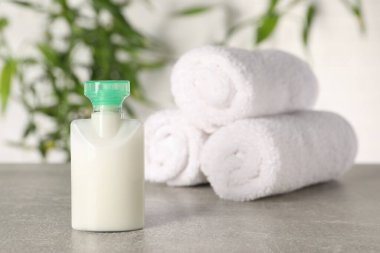 Mini kozmetik ürünler şişesi ve açık gri masaya sarılmış havlular bulanık arka planda.