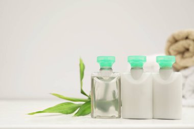 Mini şişeler dolusu kozmetik ürünler ve beyaz masanın üzerinde yeşil bir dal. Metin için boşluk