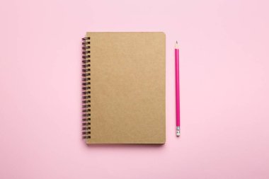 Pembe arkaplandaki defter ve kalem, üst görünüm