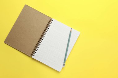 Sarı arka planda defter ve kalem, üst manzara. Metin için boşluk