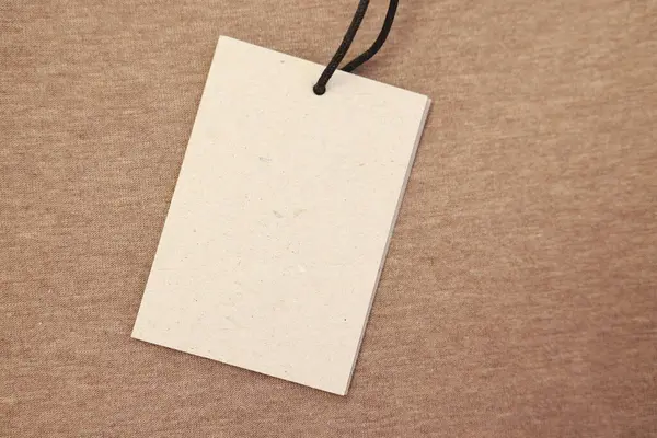 Cardboard tag on brown garment, top view. Space for text