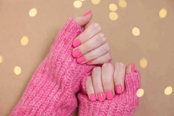 Woman showing her manicured hands with pink nail polish on dark beige background, top view. Bokeh effect