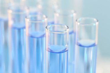 Laboratuvar analizi. Bulanık arkaplanda açık mavi sıvı bulunan birçok cam test tüpü, yakın plan