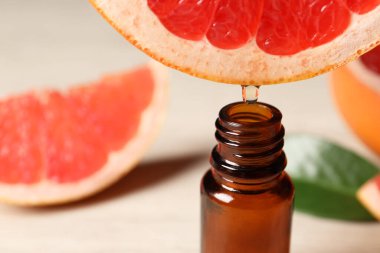 Temel yağ, arka planda hafif arkaplanda greyfurttan şişeye damlıyor.