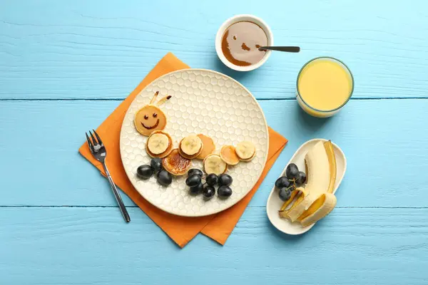 Creative serving for kids. Plate with cute caterpillar made of pancakes, grapes and banana on light blue wooden table, flat lay