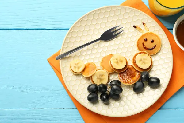 Creative serving for kids. Plate with cute caterpillar made of pancakes, grapes and banana on light blue wooden table, flat lay. Space for text
