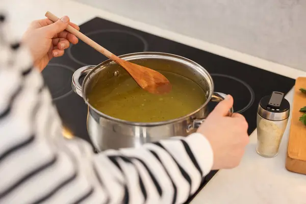 Woman with wooden spoon cooking soup in kitchen, closeup
