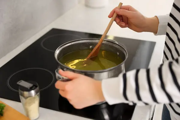 Woman with wooden spoon cooking soup in kitchen, closeup