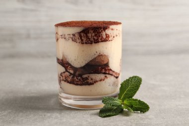 Cam içinde nefis tiramisu ve gri desenli masada nane şekeri, yakın plan.