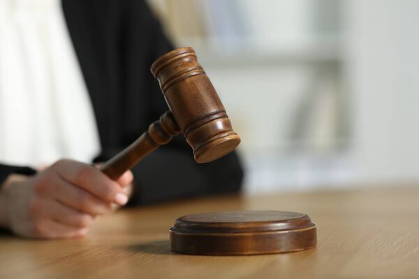 Судья бьет молотком по деревянному столу в зале суда, крупным планом. Пространство для текста