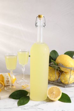 Lezzetli limoncello likörü, limonlar ve yeşil yapraklar beyaz mermer masada.