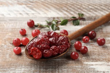 Lezzetli kuru kızılcıklar kaşıkta ve taze olanlar kırsal ahşap masada, yakın plan.