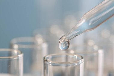 Laboratuvar analizi. Bulanık arkaplanda, pipetten cam test tüpüne sıvı damlatıyor. Metin için boşluk