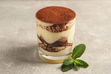 Cam içinde nefis tiramisu ve gri desenli masada nane şekeri, yakın plan.