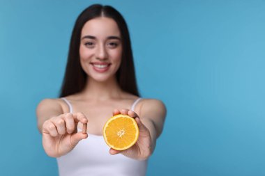 Vitamin hapı ve açık mavi arka planda bir parça turuncu, seçici odaklı güzel bir genç kadın. Metin için boşluk