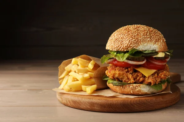 Delicious burger with crispy chicken patty and french fries on wooden table. Space for text