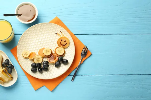 Creative serving for kids. Plate with cute caterpillar made of pancakes, grapes and banana on light blue wooden table, flat lay. Space for text