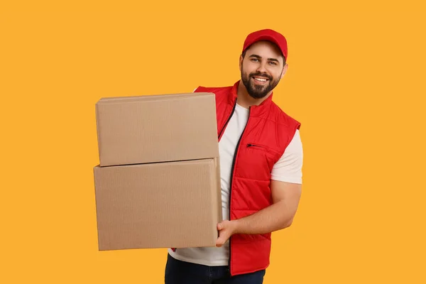 Happy young courier with parcels on orange background