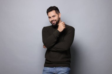 Gri arka planda şık süveter giyen mutlu adam.