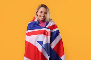 Turuncu arka planda Birleşik Krallık bayrağı taşıyan mutlu kadın.