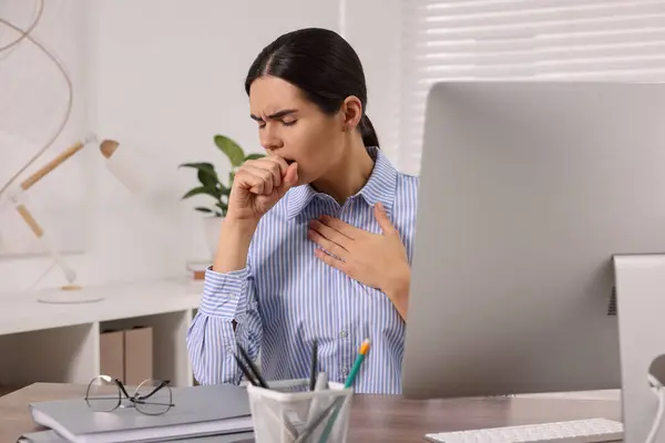 Woman coughing at table in office. Cold symptoms