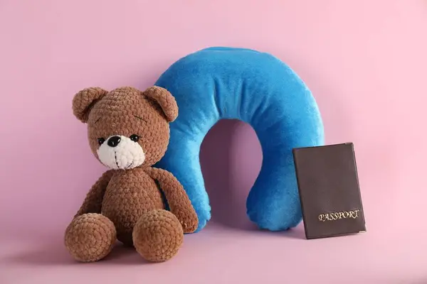 Light blue travel pillow, toy bear and passport on pink background