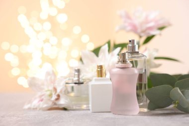 Güzel zambak çiçekleri buketi ve parfüm şişeleri bej arka planda bulanık ışıklarla, yakın plan. Metin için boşluk