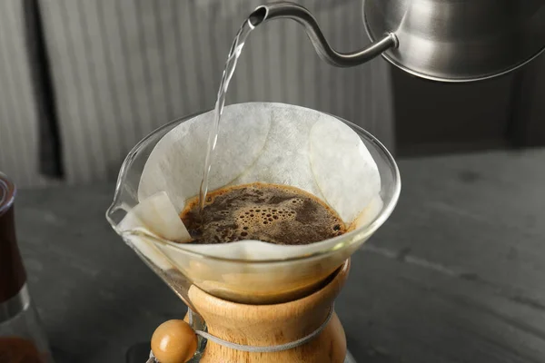stock image Pouring hot water into glass chemex coffeemaker with paper filter and coffee on gray table, closeup