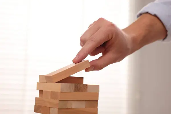Playing Jenga. Man Building tower with wooden blocks, closeup