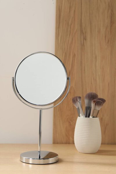 Mirror and makeup brushes on wooden dressing table in room