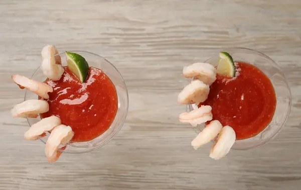 Tasty shrimp cocktail with sauce and lime in glasses on wooden table, flat lay